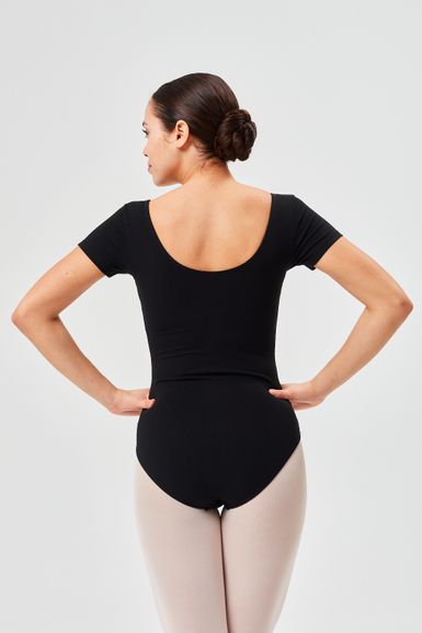 Eine Frau in einem schwarzen Trikot und hellen Strumpfhosen steht mit abgewandtem Gesicht da