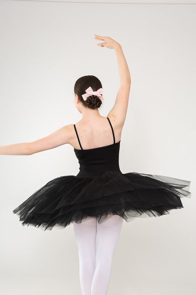 Balletttänzerin in schwarzem Tutu und weißen Strumpfhosen posiert mit erhobenem Arm