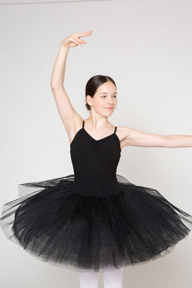 Eine junge Ballerina in einem schwarzen Tutu posiert mit erhobenem Arm.