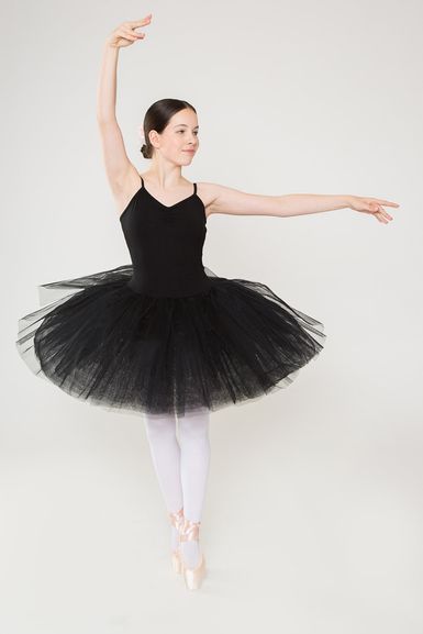 Balletttänzerin in einem schwarzen Tutu und Spitzenschuhen posiert mit einem erhobenen Arm und einem ausgestreckten Bein.