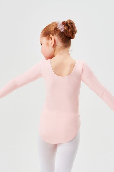 Ein junges Mädchen in einem rosa Trikot und weißen Strumpfhosen steht mit ausgestreckten Armen da und blickt von der Kamera weg.