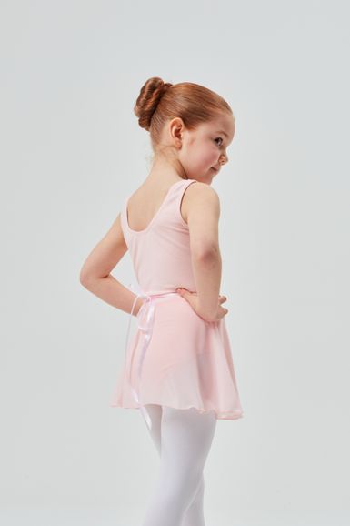 Ein junges Mädchen in einem rosa Ballett-Outfit und weißen Strumpfhosen steht mit den Händen in den Hüften und schaut zur Seite.
