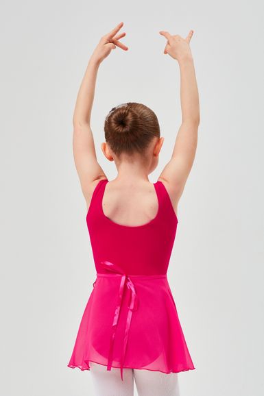 Ein junges Mädchen in einem rosa Ballett-Outfit steht mit erhobenen Armen und blickt von der Kamera weg.