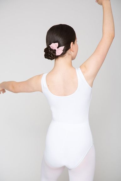 Eine Person in einem weißen Ballettbody und einer rosa Schleife tanzt mit erhobenen Armen
