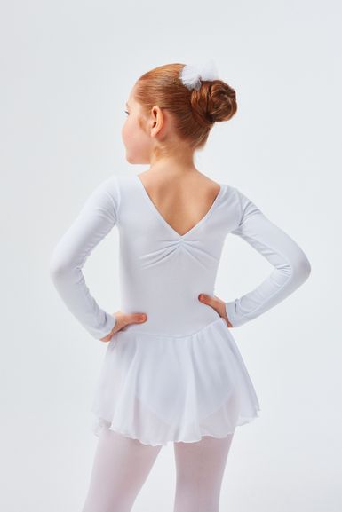 Ein junges Mädchen in einem weißen Ballett-Outfit steht mit den Händen in den Hüften und blickt von der Kamera weg.