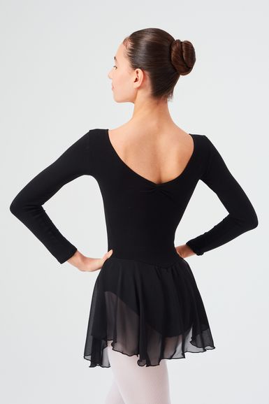 Eine Balletttänzerin in einem schwarzen Ballettbody und Rock posiert mit den Händen in den Hüften und blickt von der Kamera weg.