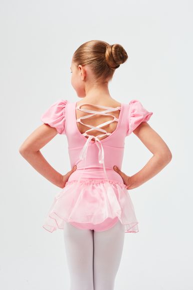 Ein junges Mädchen in einem rosa Ballettkostüm steht mit den Händen in den Hüften und blickt von der Kamera weg.