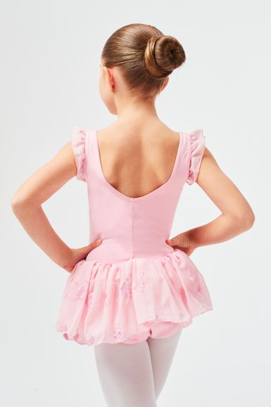 Ein junges Mädchen in einem rosa Ballett-Outfit steht mit den Händen in den Hüften und blickt von der Kamera weg.