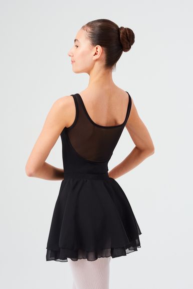 Eine junge Frau in einem schwarzen Ballettanzug und Rock steht mit den Händen in den Hüften und blickt nach links.