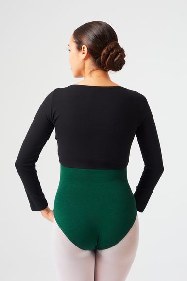 Eine Frau mit dunklem Haar zu einem Dutt trägt ein schwarzes Langarmoberteil und einen grünen Ballettanzug und blickt von der Kamera weg.