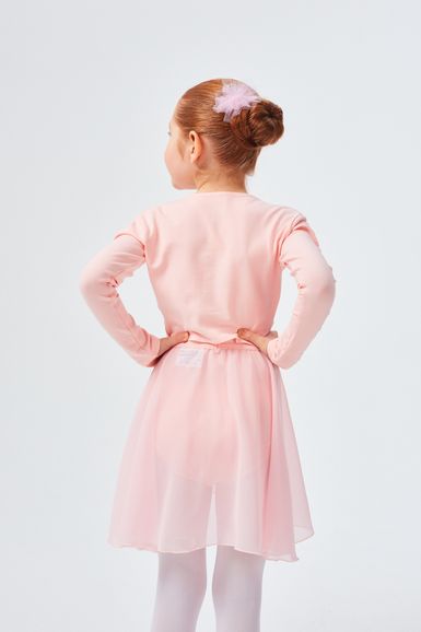 Ein junges Mädchen in einem rosa Ballett-Outfit steht mit den Händen in den Hüften und blickt von der Kamera weg.