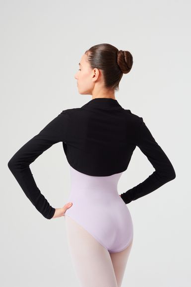 Eine Frau in einem lavendelfarbenen Trikot und einem schwarzen Langarmoberteil steht mit den Händen in den Hüften und blickt von der Kamera weg.