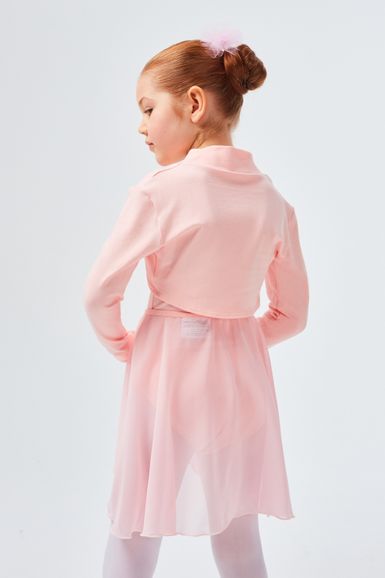 Ein junges Mädchen in einem rosa Ballettkleid und weißen Strumpfhosen steht mit dem Rücken zu einem schlichten weißen Hintergrund.