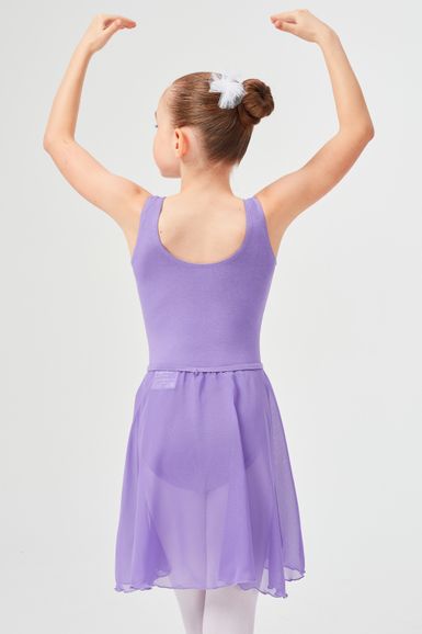 Ein junges Mädchen in einem lavendelfarbenen Ballettkleid und Dutt steht mit erhobenen Armen da und blickt von der Kamera weg.