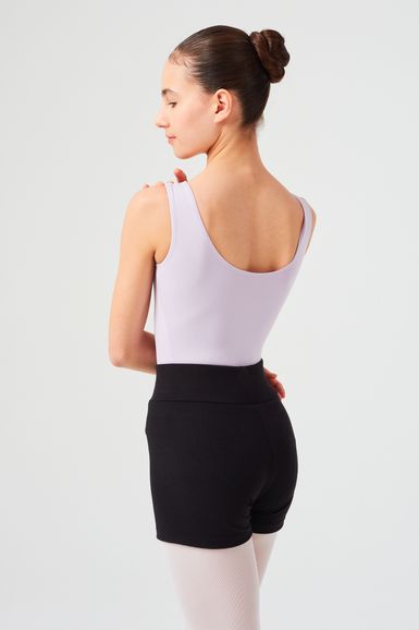 Eine junge Frau in einem lavendelfarbenen Trikot und schwarzen Shorts steht mit abgewandtem Gesicht da und hat ihr Haar zu einem Dutt gebunden.