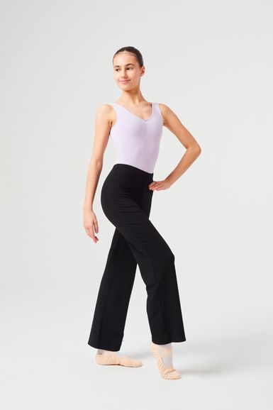 Eine Frau in einem hellvioletten Trikot und einer schwarzen Hose posiert in Ballettschuhen.