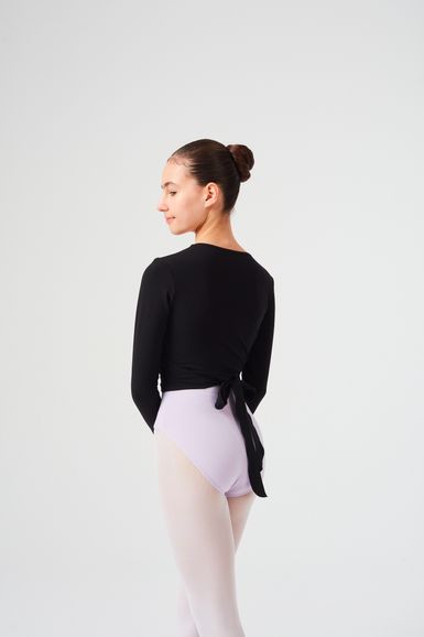 Eine junge Balletttänzerin in einem schwarzen Wickeltop und einem lavendelfarbenen Ballettbody steht im Profil.