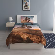 Frontansicht eines Motocross‑Bettwäsche‑Sets mit Fahrer im Sprung vor staubiger Landschaft. Kissen und Decke im passenden Dirtbike‑Design.