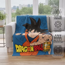 Blaue Dragon Ball Super Decke ausgebreitet auf einer grauen Couch im Wohnzimmer; am rechten Bildrand sind vier Eigenschafts-Icons mit den Texten „100% Polyester“, „100% Qualität“, „Atmungsaktiv“ und „Pflegeleicht“ zu sehen.