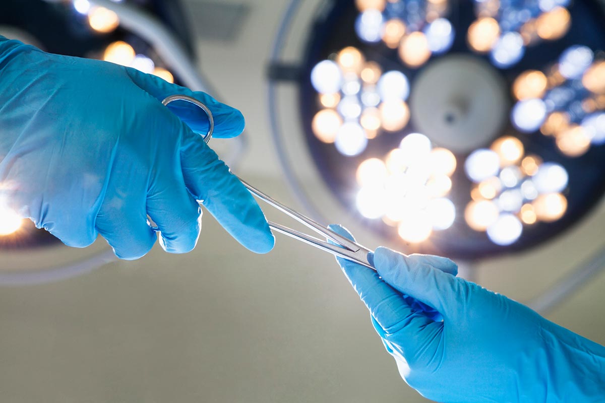 Sterile Einmalhandschuhe im OP Hände in Einmalhandschuhen reichen sich eine OP-Schere – Einmalhandschuhe im OP-Bereich müssen steril sein