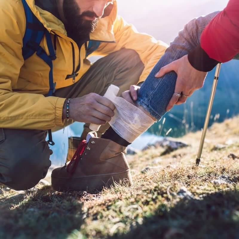Erste Hilfe Tasche eignen sich für Outdooraktivitäten wie Wanderungen Ein Mann verbindet einer Frau den Knöchel mit einem Verband aus einer Erste Hilfe Tasche