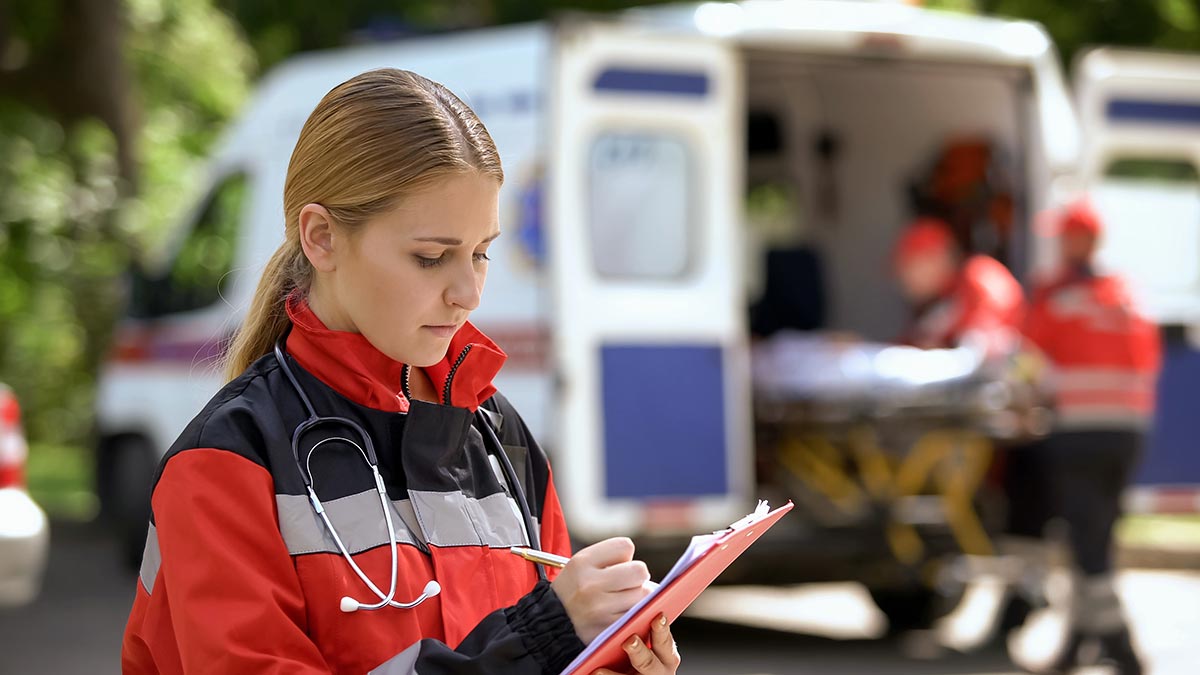 Organisationsmittel Notfalleinsatz Notfallsanitäterin notiert vor Ambulanz mit Stift auf Klemmbrett Informationen – Organisationsmittel erleichtern solche Vorgänge