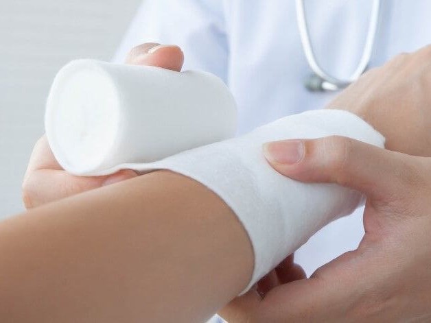 Verbandstoffe aus dem Praxisbedarf Ein Arzt verbindet die Hand eines Patienten mit Verbandstoffen aus dem Praxisbedarf