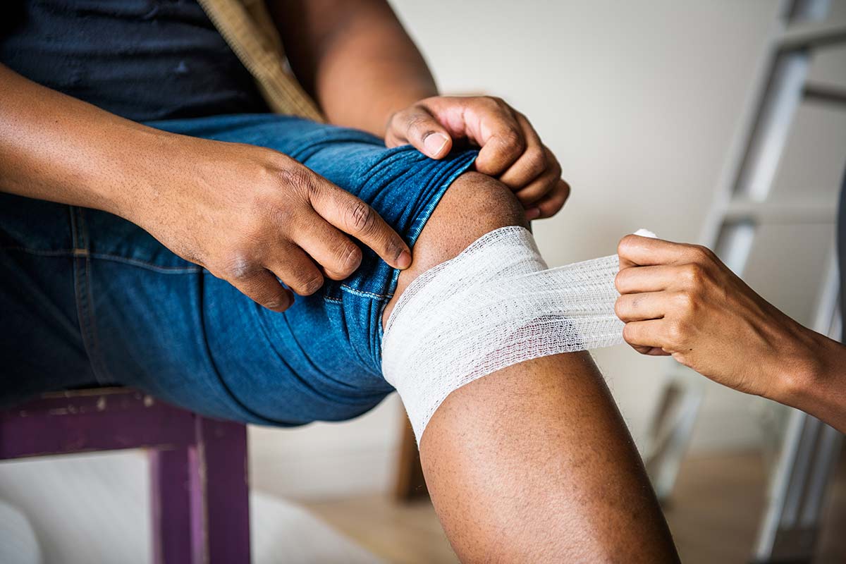 Material aus dem Verbandkasten Nachfüllset Frau verbindet das Knie eines Mannes mit Bandage aus einem Verbandkasten Nachfüllset
