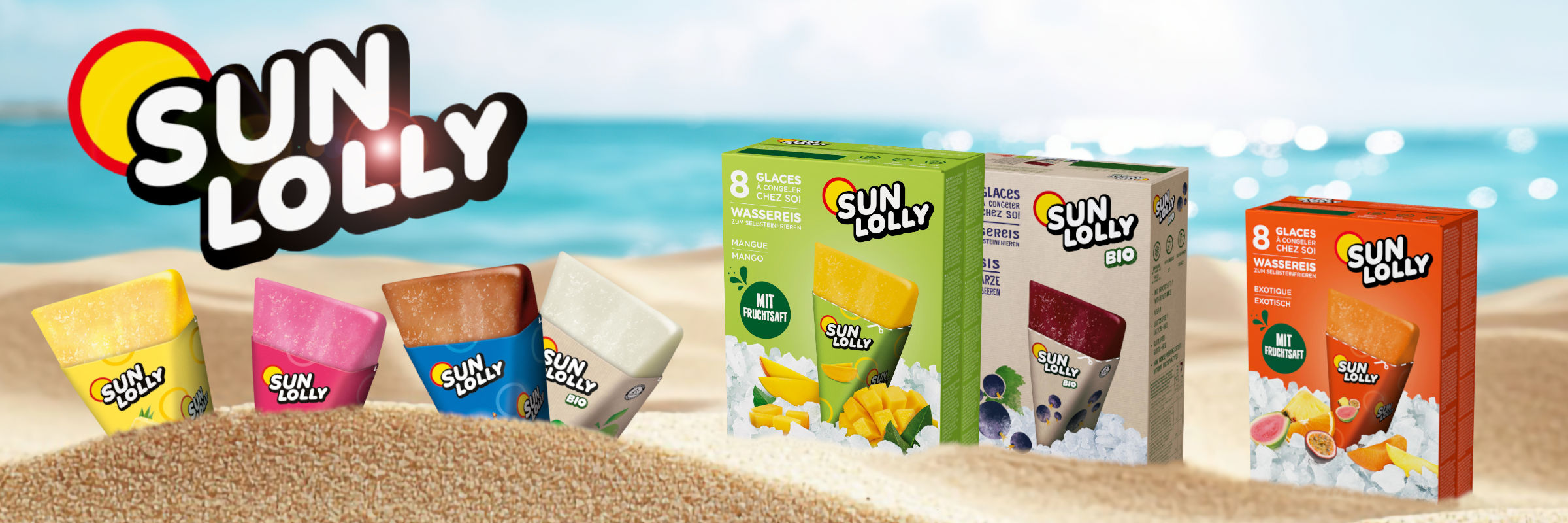 Das Bild zeigt ein Werbebanner für „Sun Lolly“-Wassereis. Auf der linken Seite befindet sich das große, schwarz-weiße „Sun Lolly“-Logo mit einer gelb-roten Sonne im Hintergrund. Davor liegen vier ausgepackte, dreieckige Wassereise in den Farben Gelb, Pink, Braun und Weiß im Sand. Rechts daneben stehen drei verschiedene Verpackungskartons der Geschmacksrichtungen Mango, Schwarze Johannisbeere und Exotic, jeweils umgeben von Eiswürfeln und frischen Früchten. Im Hintergrund ist ein unscharfer Strand mit blauem Meer und Himmel zu sehen.