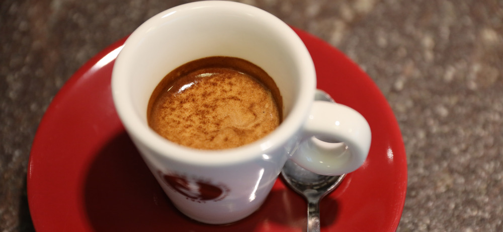  Italienischer Espresso mit dichter goldbrauner Crema in weißer Tasse auf roter Untertasse 