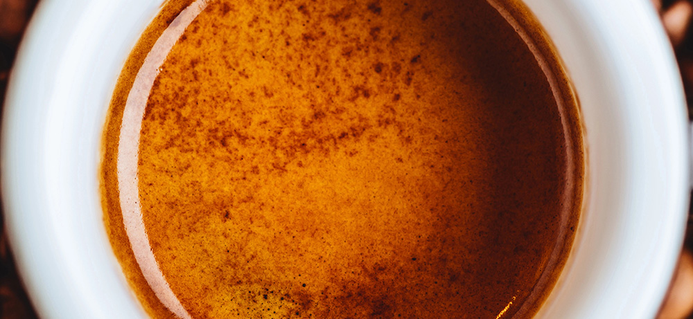 Warum viel Crema nicht automatisch guten Geschmack bedeutet Kleine weiße Espressotasse mit goldbrauner Crema auf einem Holztisch mit einzelnen Kaffeebohnen