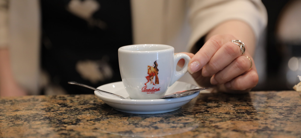 Espresso bei Barbera in Neapel — Carmen, die Exportleiterin, in der hauseigenen Bar der Rösterei Espressotasse mit Barbera-Logo in der Hand einer Mitarbeiterin in der Barbera-Rösterei in Neapel