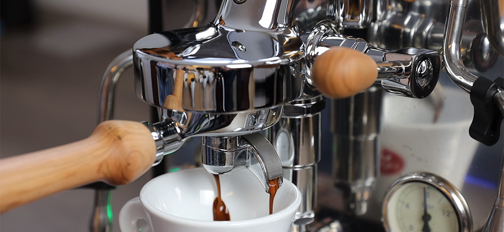 Espresso am Siebträger Verchromte Hebel-Siebträgermaschine zieht einen Espresso mit dichter Crema in eine weiße Tasse