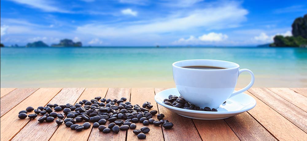  weisse Kaffeetasse mit Kaqffeebohnen im Hintergrund Strand und Meer 