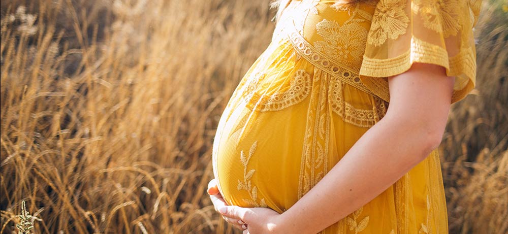  Schwangere Frau in gelbem Kleid auf sonnigem Feld 