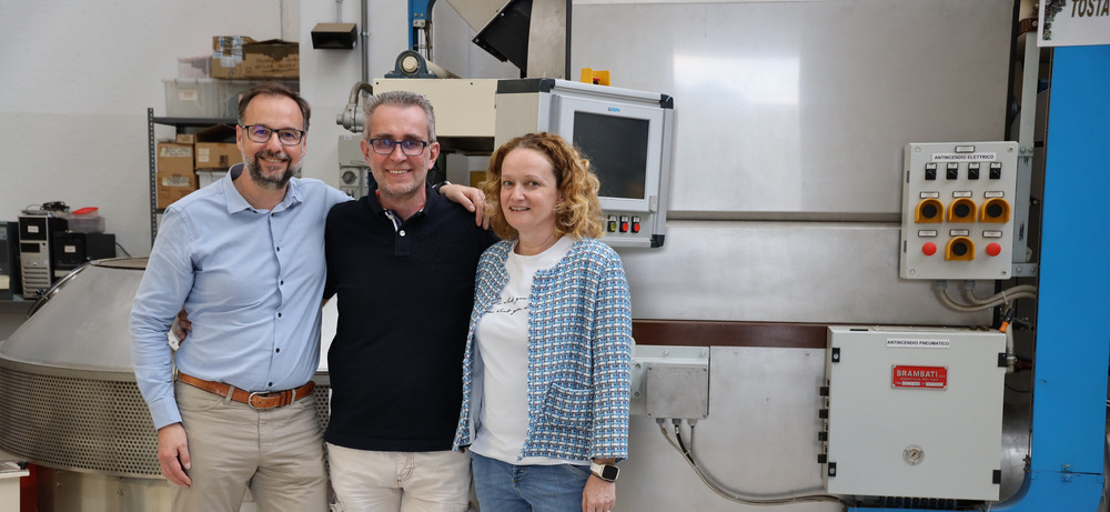 Walter Gefäll mit Lorenzo Martinelli (Geschäftsführer) und Elena Martinelli (Exportleiterin) vor der Röstanlage Tustadora in Arco Walter Gefäll mit Lorenzo und Elena Martinelli vor der Tustadora-Röstanlage in der Omkafe-Produktion in Arco