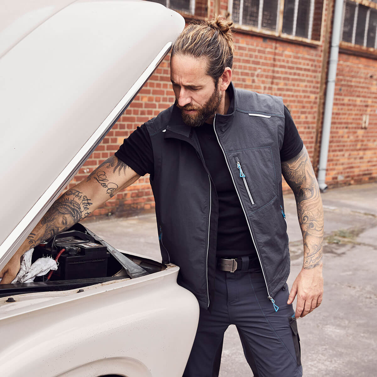 Ein Mann in Arbeitskleidung von Terrax Workwear steht vor einer geöffneten Motorhaube