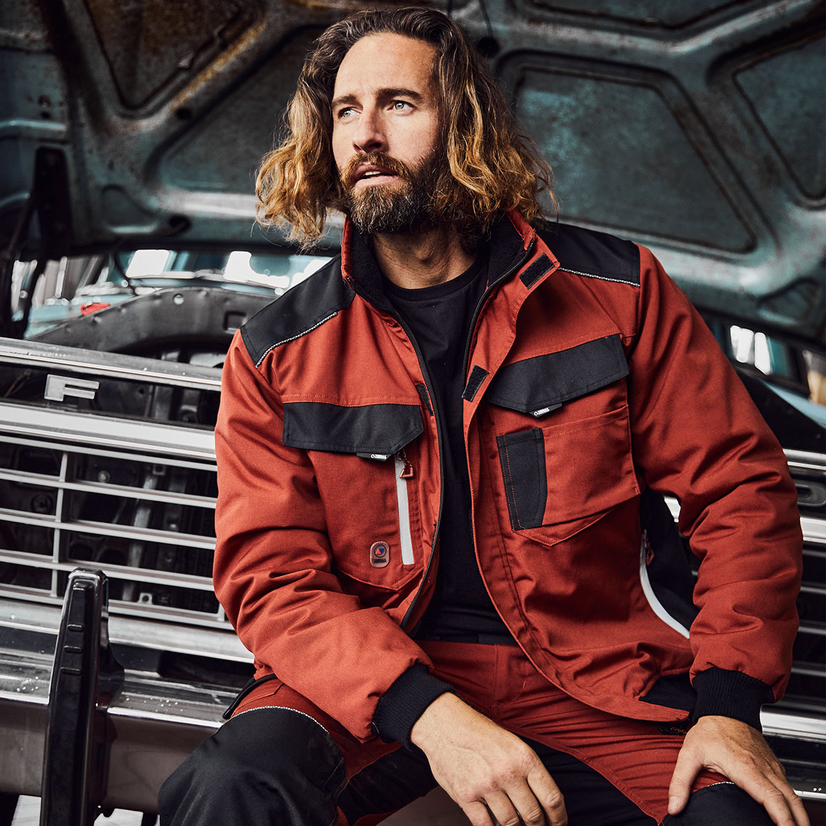 Sitzender Mann mit einer Pilotenjacke von Terrax Workwear vor einem Auto
