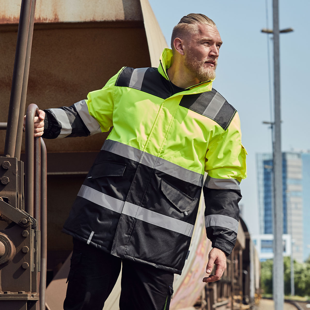 Mann mit einer Warnschutzjacke von Terrax Workwear lehnt sich aus einem Zug-Waggon und hält sich mit einer Hand fest