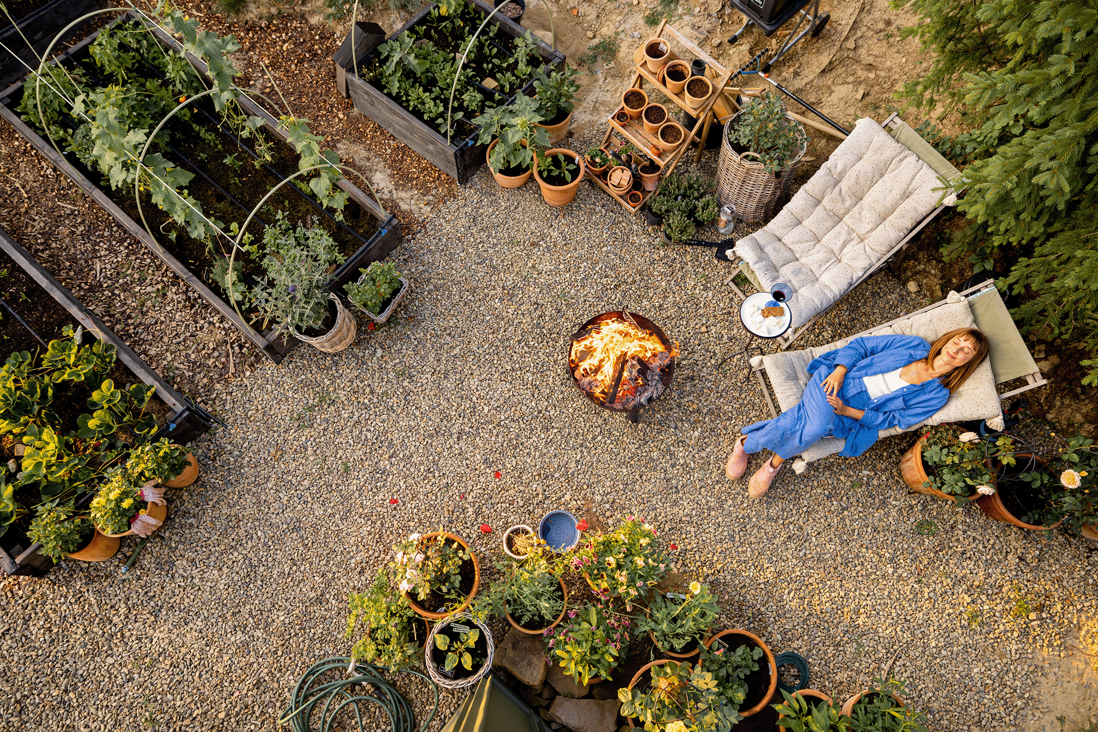Dame entspannt auf einer Liegen in ihrem Garten neben Feuerschale