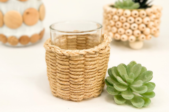 Verschiedene gebastelte Blumenübertöpfe: zwei Gläser sind beklebt mit Holzknöpfen und ein Glas ist umwebt mit Garn