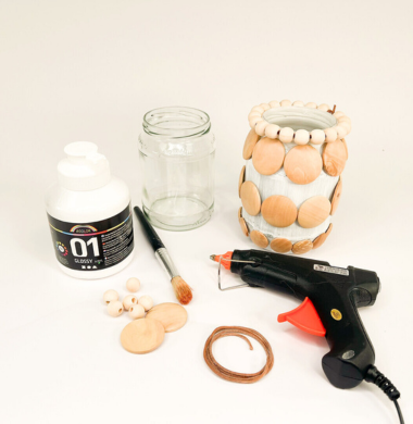 Mit Holzknöpfen verziertes Glas und die benötigten Materialien daneben: Weiße Glanzfarbe, Holzknöpfe, Pinsel, Glas, draht und eine Heißklebepistole.