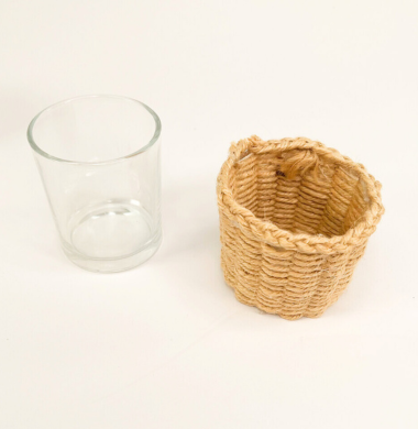 Ein Glas und daneben der Pappbecher der mit Jutegarn bewebt worden ist.