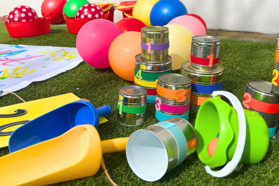Verschiedene selbstgebastelte Spiele liegen verstreut herum:bemalte Moosgummi-Zielscheiben, kleine bunte Sandschsufeln, Dosen mit Moosgummi-Zahlen, Luftballons und Spielbälle.