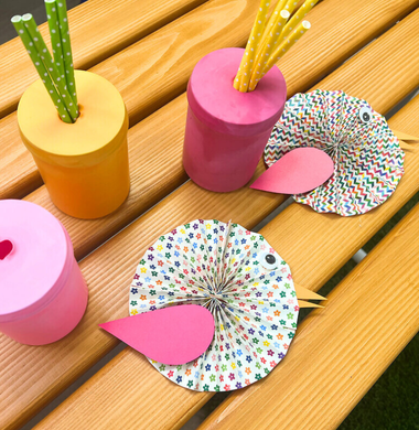 Sommerliche Deko: Strohhalmhalter aus einem Glas, das mit einem bunten luftballon überzogen wurde und Vögel aus buntem Papier.