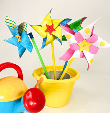 Eine bunte Gießkanne und bunte Windräder die in einem gelben Eimer stehen.
