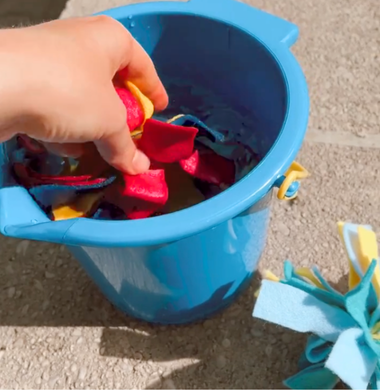 Eine Hand drückt Bastelzilzreste, die zusammen gebunden sind, in einen mit Wasser gefüllten Eimer.
