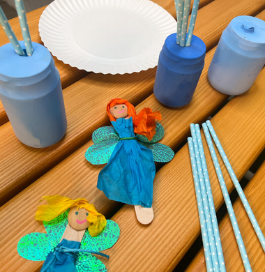 Auf einem Tisch liegene verschiedene Basteleien: Feen aus Holzstäbchen und Papier sowie Gläser, die in einem Luftballon gehüllt worden sind.