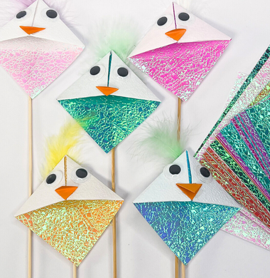 Faltpapier-Vögelchen aus glänzenden Papier und Holzstäbchen.