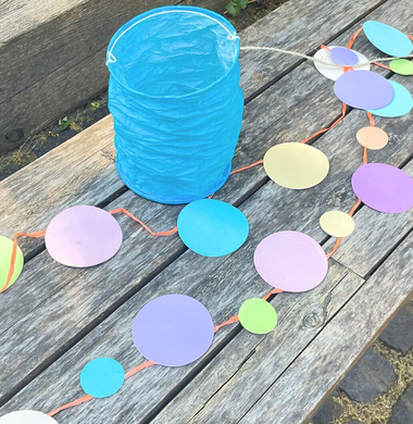 Sommerliche Girlande aus bunten Papierkreisen, die durch eine Schnur verbunden sind und einer blauen Crash-Laterne